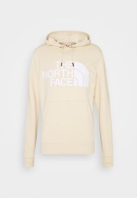 Krémová mikina s kapucí vyrobená z měkkého materiálu, s velkým bílým logem "THE NORTH FACE" na přední straně, klokaní kapsou a nastavitelnou kapucí.