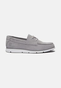 Scarpa da barca in suede grigia con suola in gomma bianca, caratterizzata da dettagli con lacci e accenti di cucitura. Logo impresso sul lato.