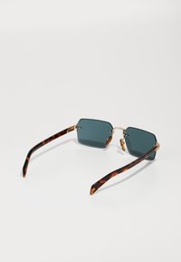 Ochelari de soare hexagonali cu lentile verzi închise. Brațe cu model țestoasă și accente aurii pe ramă, evidențiind un design elegant.