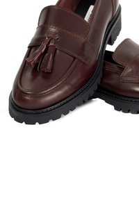 Burgundy leather loafers with a smooth finish, featuring a decorative tassel and a black rubber sole with a rugged tread pattern.