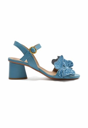 Sandalo in pelle blu con tacco basso, cinturino alla caviglia e fibbia dorata, con applicazioni decorative di farfalle blu sulla fascia frontale.