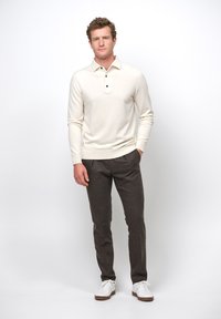 Crème lange mouwen polo met drie zwarte knopen, gecombineerd met donkergrijze op maat gemaakte broek en witte sneakers. Eenvoudige en gladde texturen.