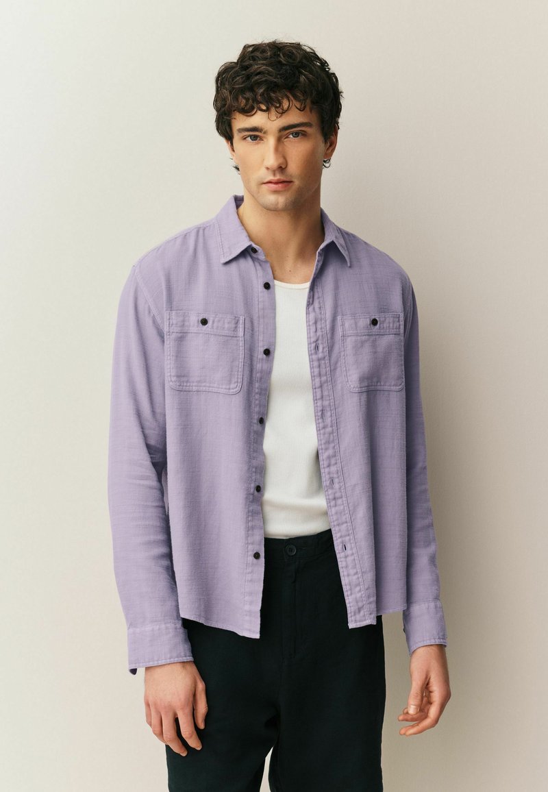 Hele lilla trukidega nööpidega särk, millel on kaks rinnataskut, mustad nupud ja pikad varrukad. Kandmiseks valge topp ja mustad püksid.