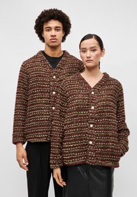 Textúrované kardigány s pruhmi v burgundskej a zelenej farbe, vo voľnom strihu, s výstrihom do V a veľkými gombíkmi, nosené dvoma modelkami.