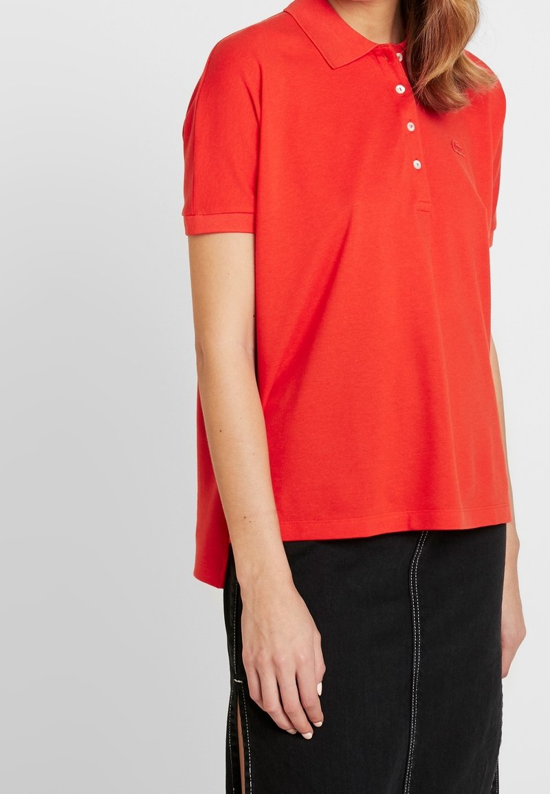 Röd polo skjorta med klassisk krage, korta ärmar och treknappsstängning. Mjukt tyg med en liten broderad logotyp på bröstet.