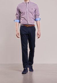 Röd- och vitrutig skjorta med uppknäppt krage, ljusblå manschetter, marinblå chinos, brun läderbälte och marinblå sneakers.