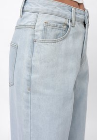Light blue denim jeans featuring a high waist, straight-leg design, and visible stitching details with five pockets. The fabric has a soft texture.