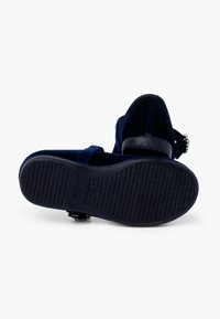 Sandalias azul marino con una textura suave, correa ajustable y una suela plana de goma con un patrón de agarre texturizado. Detalle de hardware en plata incluido.