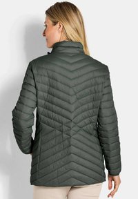 Donkergroene pufferjack met een hoge kraag, voorzien van een chevron-quiltpatroon en ribbelmouwen. Lichtgewicht stof met een gladde textuur.