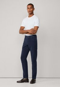 Navy chino's met een rechte snit, voorzien van een gladde textuur, zijzakken en een ritssluiting, gecombineerd met een effen wit T-shirt en donkere schoenen.
