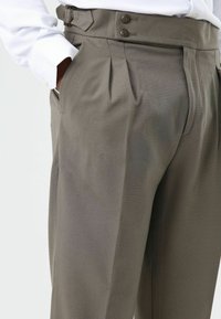 Pantalon gris sur mesure en tissu texturé, avec deux plis à l'avant, une fermeture à double bouton et des poches latérales.