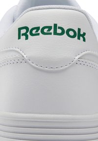Valkoiset tennarit, joissa on sileä nahka-alaosa ja vihreä "Reebok"-logo kantapäässä, pyöreä muoto ja näkyvät saumat sivuilla.