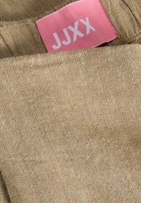 Μπεζ υφασμάτινη υφή με μια ροζ ετικέτα ρούχου ραμμένη εσωτερικά που δείχνει το "JJXX" με άσπρα γράμματα.