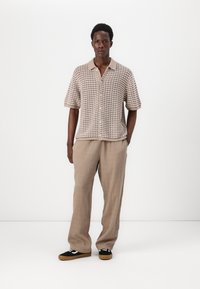 Knit short-sleeve shirt in beige with a textured pattern, paired with loose-fitting beige pants and black sneakers with white accents.