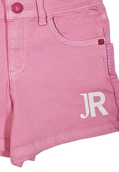Gli shorts di jeans rosa presentano una chiusura con bottone, tasche frontali e un logo bianco "JR". La texture appare liscia con bordi cuciti e un'etichetta a forma di fiore.