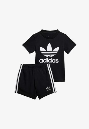 Maglietta nera in cotone con logo Adidas bianco e design grafico. Pantaloni corti neri coordinati con strisce laterali bianche e dettaglio del logo.