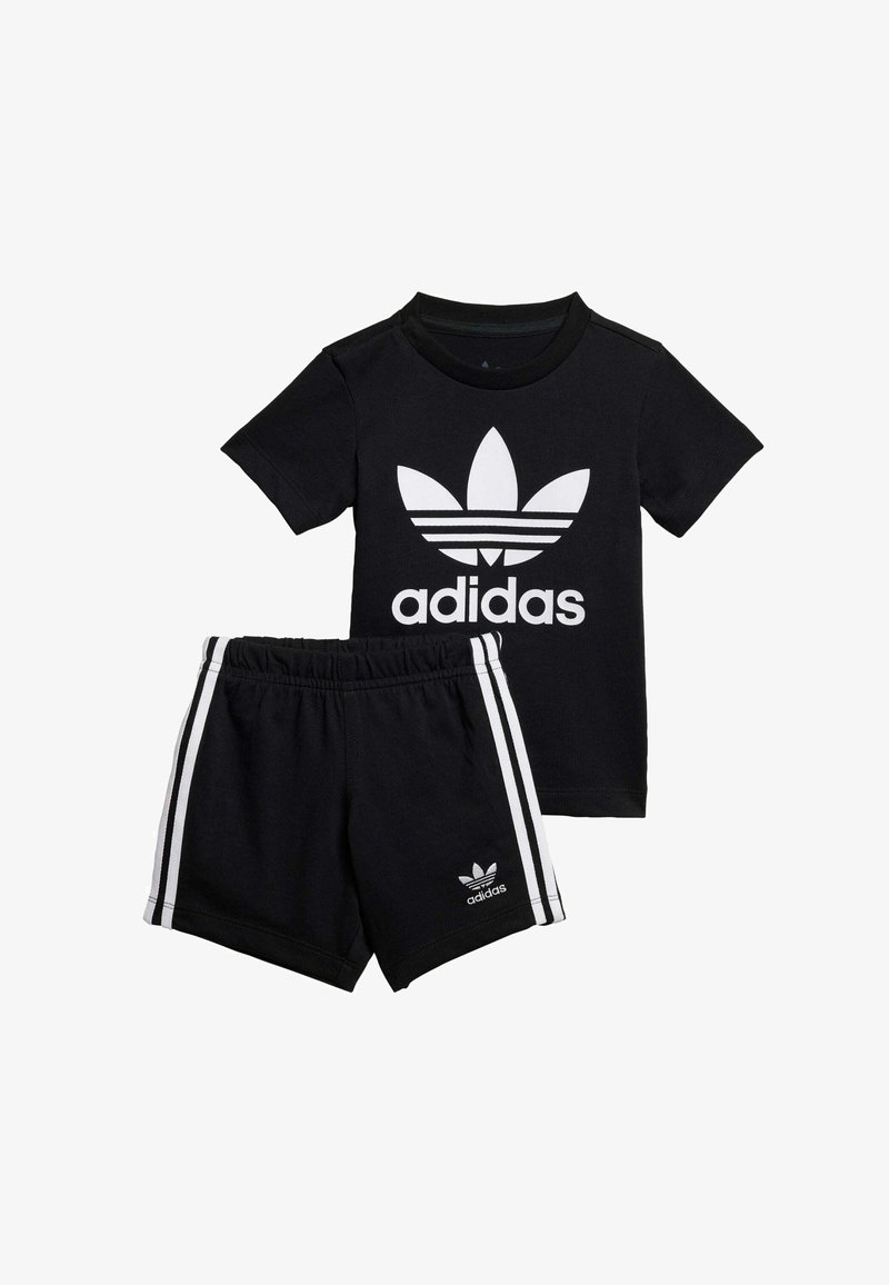 Maglietta nera in cotone con logo Adidas bianco e design grafico. Pantaloni corti neri coordinati con strisce laterali bianche e dettaglio del logo.