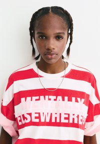 Rot-weiße gestreifte Oversize-T-Shirt mit dem Text "MENTALLY ELSEWHERE", begleitet von einer silbernen Kettenhalskette.