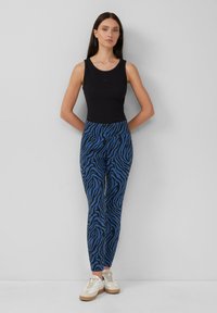 Zwarte tanktop, blauwe zebra-print legging, slim fit ontwerp, zachte stof, witte sneakers, minimalistische stijl, staand tegen een lichte achtergrond.