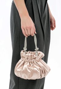 Helle rosa Satin-Handtasche mit gerafftem Design, silbernen geflochtenen Griffen und einem geknoteten Akzent, gehalten von einer Hand neben dunkelgrauen Hosen.