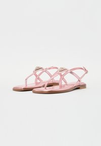 Rosa metalliska sandaler med platt sula och design med korsade remmar. Har en dekorativ guldaccent på remmen. Slät textur.