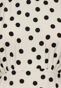Tissu blanc avec taille froncée présentant un motif uniformément espacé de gros pois noirs.