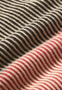 Striped fabric in black and cream tones layered over red and cream stripes. Textured wool with visible stitches and a soft, fuzzy appearance.