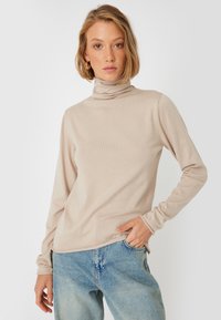 Pull en col roulé beige en tissu doux, avec des manches longues et une coupe décontractée, associé à un jean en denim bleu clair.