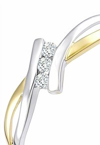 Aukso ir sidabro atspalvių žiedas su trimis skaidriais akmenimis, turintis lygią, išlinkusią formą ir blizgius paviršius.