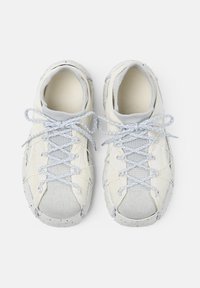 Sneaker bianche e grigie chiaro in tessuto a maglia, con suole macchiate e lacci grigi riflettenti legati a fiocco, viste dall'alto su uno sfondo bianco.