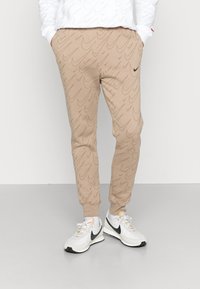 Pantalones jogger beige con un patrón de olas texturizado, con cintura y puños elásticos; combinados con zapatillas deportivas blancas y negras.