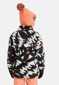 Kurtka polarowa w czarno-białym oszałamiającym wzorze, z czerwonymi akcentami, kołnierzem i miękką teksturą, zestawiona z różowym, dzierganym beanie.