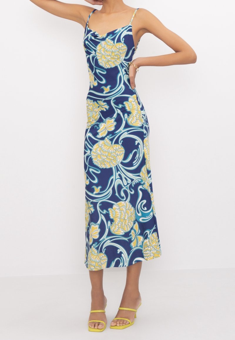 Robe sans manches bleu marine avec un motif floral jaune et des accentuations tourbillonnantes. Le tissu a une texture lisse, longueur au genou avec une silhouette ajustée.