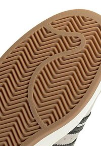 Semelle de sneaker en caoutchouc avec un motif en zigzag, présentant une base marron et des murs latéraux blancs. Texturée pour une meilleure adhérence et stabilité.