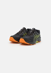 Scarpe da corsa nere con accenti arancioni e verdi, dotate di suole testurizzate, tessuto in rete e dettagli riflettenti. Progettate per il comfort e la presa.