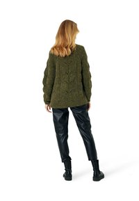 Gruby oliwkowozielony sweter z teksturowanymi wzorami warkoczy, zestawiony z czarnymi skórzanymi spodniami i botkami, widziany od tyłu.