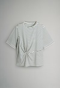 Svītrainā t-kreklā baltā un melnā krāsā, ar īsām piedurknēm un mezgla detaļu jostasvietā, kas izgatavots no mīksta, viegla auduma.