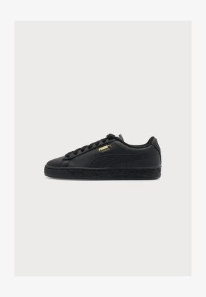Pantof sport negru Puma Suede cu talpă neagră, șireturi negre și logo Puma Suede auriu pe lateral, prezentat din partea exterioară.