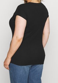 Svart ribbad stickad topp med korta ärmar, med en figurnära design som smalnar av vid midjan, i kombination med blå högmidjade jeans.