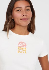 Biała bawełniana koszulka z graficznym nadrukiem przedstawiającym różową falę nad napisem "WOMEN OF THE WAVE" w kolorze pomarańczowym, okrągły dekolt.
