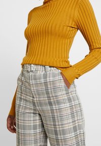 Senapsgul ribbad polokrage topp matchad med högmidjade rutiga byxor med svart, vitt och rött rutmönster. Strukturerad tyg.