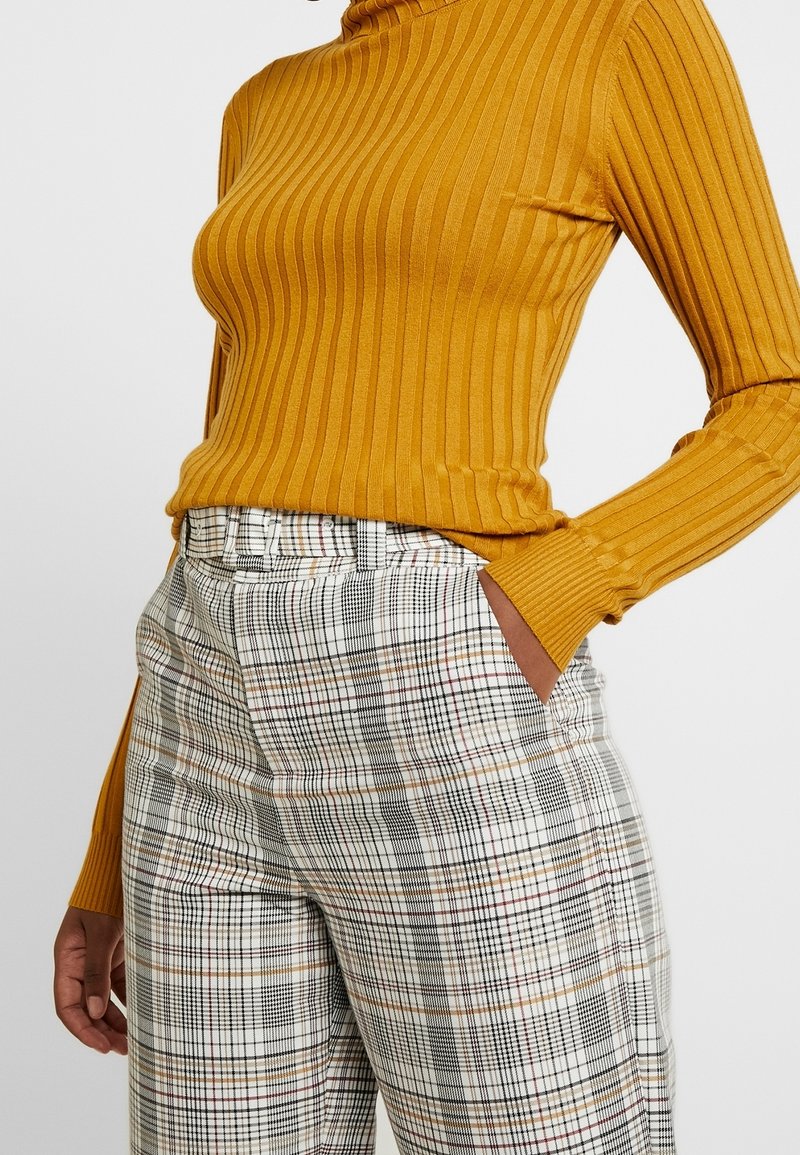 Senapsgul ribbad polokrage topp matchad med högmidjade rutiga byxor med svart, vitt och rött rutmönster. Strukturerad tyg.