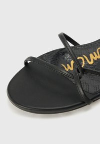 Musthave mustad, millel on pindala, kus on maonaha muster, õhukesed rihmad ja siledad, ümarad tallad. Siseservas on nähtav kullast logo.