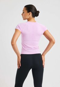 Rosa åtsittande t-shirt med korta ärmar, texturerat tyg och logotyp som är tryckt vertikalt på ryggen. Kombinerad med svarta leggings.