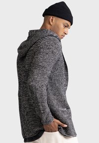 Casual, hooded sweater in a grey and black knit pattern, featuring a relaxed fit, long sleeves, and a front pocket.