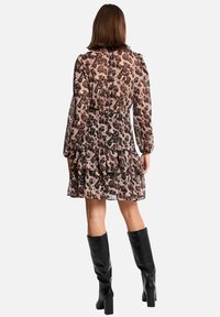 Femme portant une robe imprimée léopard à manches longues avec des volants superposés et des bottes à talons noires jusqu'aux genoux, se tenant de dos.