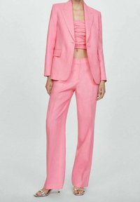 Blazer rosa a medida con un solo botón, combinado con un top corto a juego con fruncido, y pantalones de pierna ancha en una tela ligera.