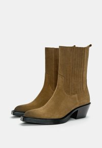 Bottines en suède marron, mi-mollet, avec des pointes pointues, des talons blocs noirs et des panneaux élastiques sur les côtés pour un enfilage facile.