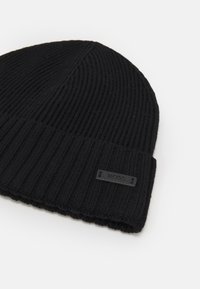 Zwarte gebreide beanie met ribbelpatroon, voorzien van een omgeslagen rand en een klein zwart leren label met het reliëf "BOSS" erop.