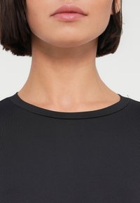 Μαύρο ριμπ τοπ με στρογγυλή λαιμόκοψη, λεία υφή και εφαρμοστή γραμμή, που τονίζει τη γραμμή του λαιμού και του γιακά χωρίς διακοσμήσεις.